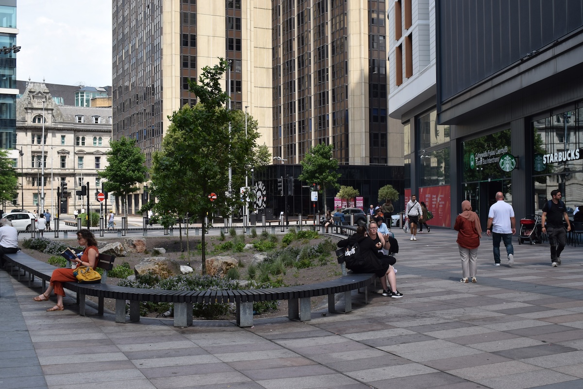 People sit around a circular rain garden in the middle of a city square