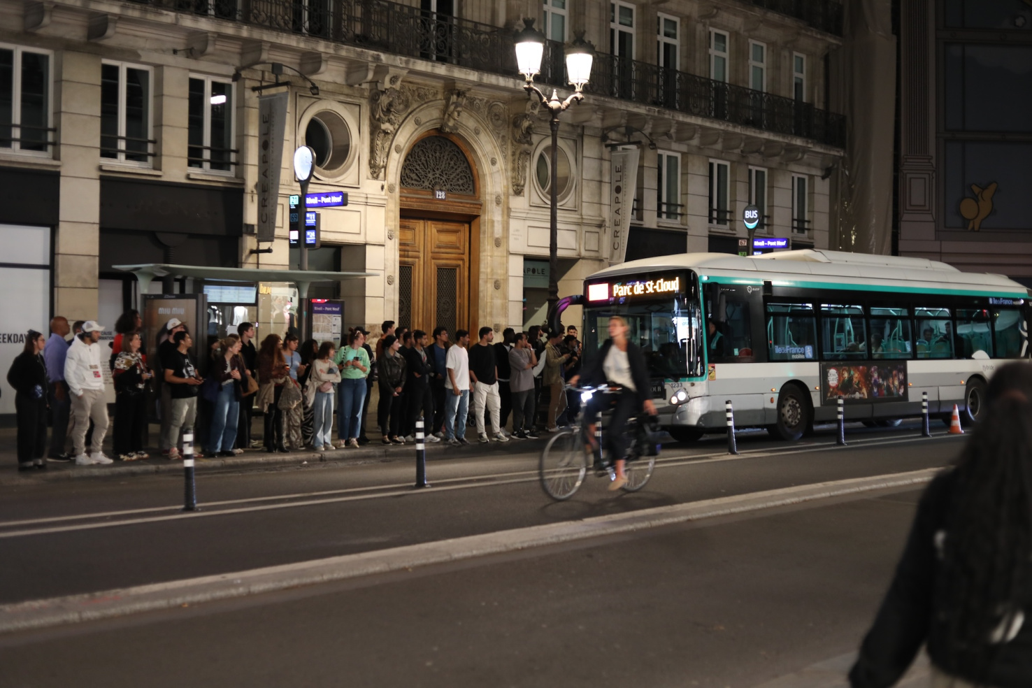 Crowd waiting for bus pulling up to station on street in Paris, France.