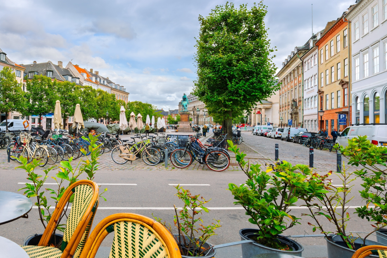 Public plaza with ample bike racks full of bikes and outdoor seating tables with folded umbrellas in Copenhagen, Denmark.