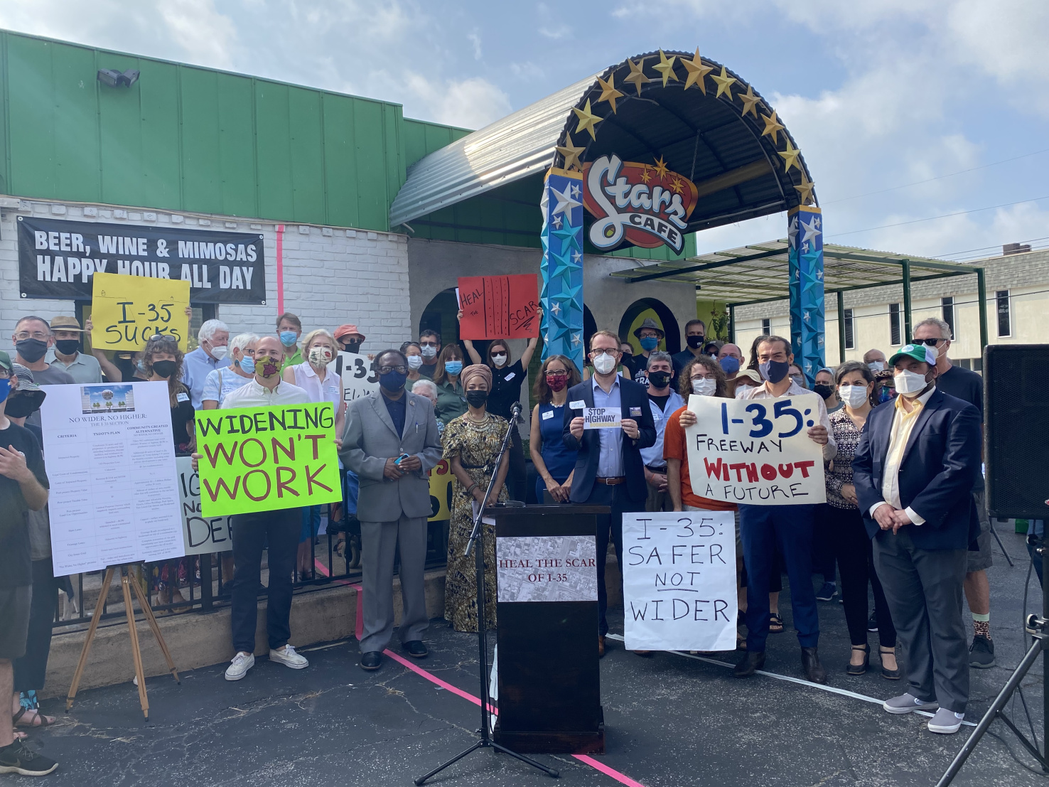A 'crowd of masked people hold signs against the widening of a highway.