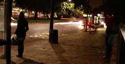 Image: A lone woman waits at a bus stop.