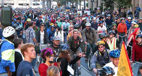 Image of hundreds of bike riders on an urban city street with people watching them ride by.