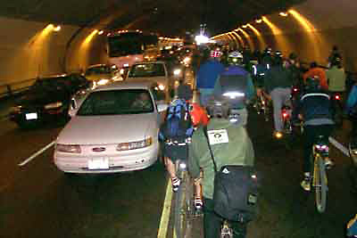 Image of many bike riders in a tunnel with cars.