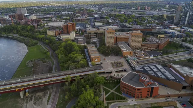 University of Minnesota Humpharey primary image of the city scape, a body of water on the left side, and a bridge running across the lower half of the image.
