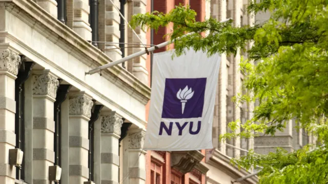 Image of the New York University Wagner white and purple flag hanging straight down with older looking buildings in the background