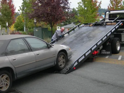 A grey car being loaded onto a flatbed truck