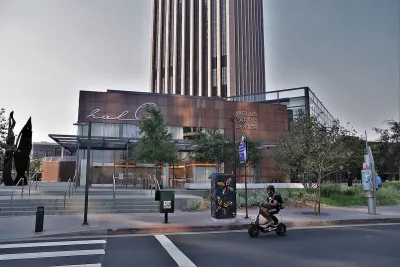 Person on small black e-bike riding on street in front of Wells Fargo Center building in Los Angeles.