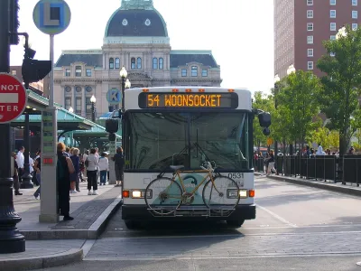 A white RIPTA bus with a bike on a front bike rack at a stop in Providence, Rhode Island.