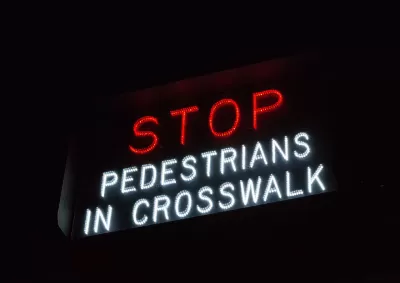 "Stop - Pedestrians in crosswalk" sign in white and red lights.