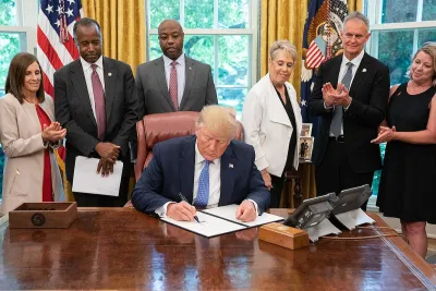 Donald Trump signing executive order in Oval Office with other officials behind him.