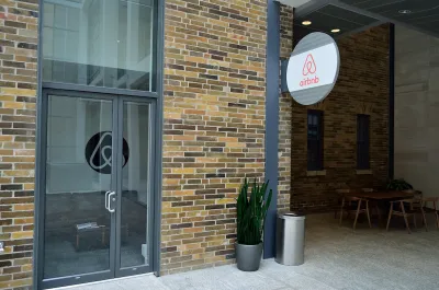 A brick building with a circular sign with the Airbnb logo hanging off of it.