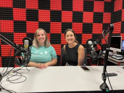 Two young women sitting in a recording studio, both caucasian, one with brown hair, one with blonde hair