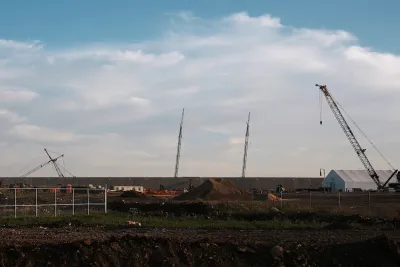 Cranes rise over a construction site on a cloudy day.