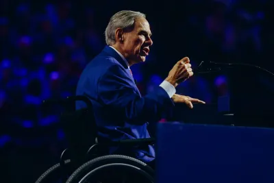 Gov. Abbot gestures with his hand at a convention. He is wearing blue and is in his wheelchair.