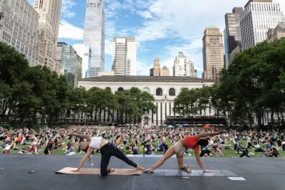 Group of people being led in yoga by two instructors on large public lawn.