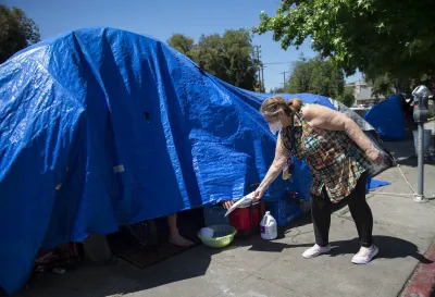 Outreach worker wearing mask reaches into blue tarp with unhoused person to hand them a pamphlet.