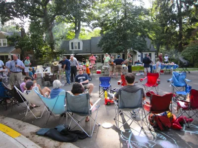 People sitting in lawn chairs on residential street having block party.