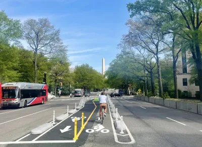 Cyclist on protected bike lane in middle of street in Washington D.C. with Washington Monument obelisk visible in background.