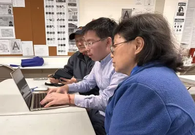 Young Chinese American man helping two seniors sign up for services on a laptop.