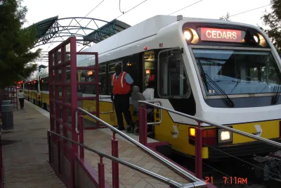 White DART light rail train at platform in Plano, Texas with conductor standing outside of door.