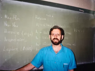 Photo of Bruce Stiftel as a young man standing in front of a green chalkboard
