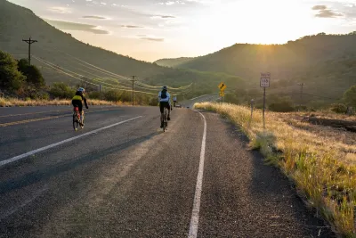 Cyclists on an empty rural paved road with hills and sunset in background.