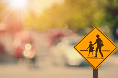 Yellow school corssing sign with two human figures against blurry background