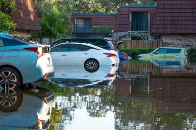 Parked cars in floodwater with two-story apartments or homes in background in Florida after hurricane.