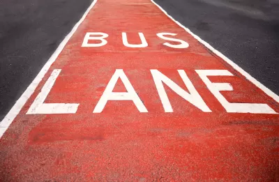 Close-up of red and white BUS LANE sign painted in street lane.