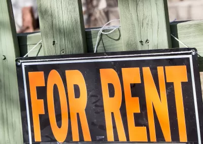 Close-up of orange and black For Rent sign on green wood fence.