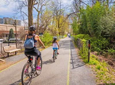 Family wearing helmets rides down separated bike trail in city.
