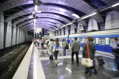 Busy subway station with people walking on platform and train stopped.