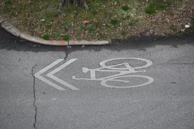 White bike sharrow symbol painted on road next to green grass.