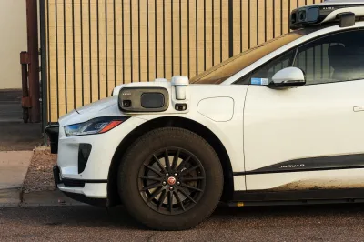 White Waymo self-driving car with camera and sensors mounted to front driver's side mirror.
