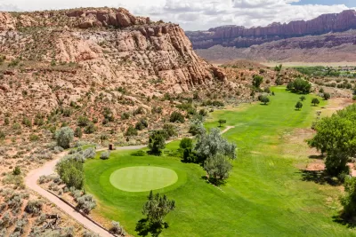 Aerial view of green colf course next to rocky desert cliffs in Moab, Utah
