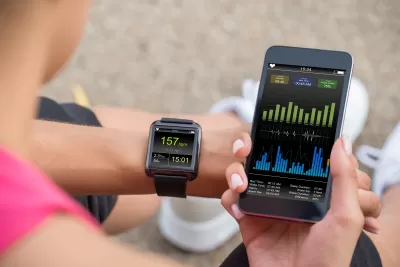 Close-up of person holding up phone and looking at their smart watch displaying fitness data