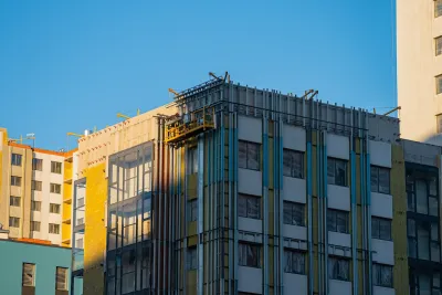 Construction workers on a suspended platform are installing thermal insulation on the facade of a modern apartment building, improving energy efficiency and reducing heat loss during cold weather.