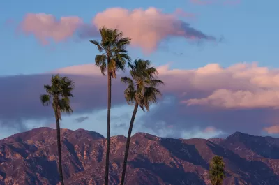 Twilight view of San Gabriel Mountains with three tall palm trees in foreground and purpleish sky.