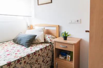 Small, brightly lit bedroom with flowery sheets on single bed in supportive housing or nursing home.