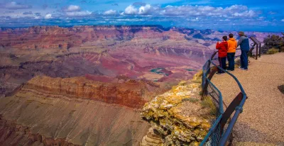 Two children and an adult looking out over railing at Grand Canyon.