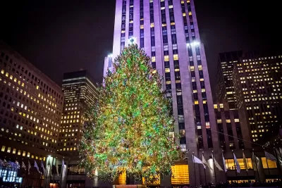 View of Rockefeller Center Christmas tree lit up at night in front of 30 Rock high-rise.
