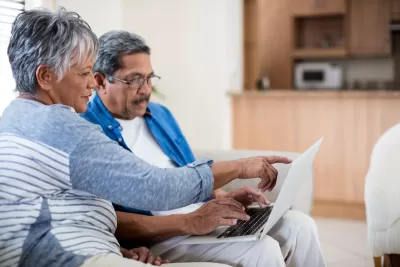 Senior couple sitting on sofa looking at laptop computer held in the man's lap.