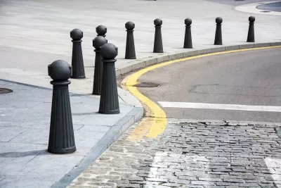Black bollards lining a curved sidewalk next to a cobblestone street.