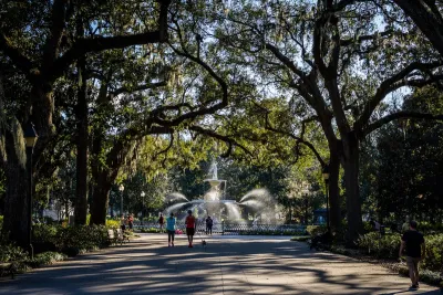 Paved path with artesian fountain at end and tall trees arching over walkway with joggers and walkers in Savannah, Georgia.