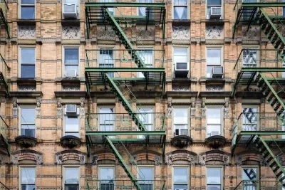 Brick New York City apartment building exterior with fire escape stairs and AC window units.