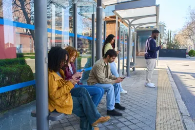 Young people at a bus stop all looking at their smartphones.
