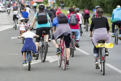 Large group of people and children on bikes in street.
