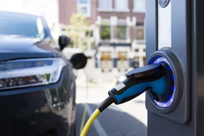 Close-up of electric car charging port with blurred dark colored car in background.