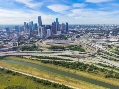 Aerial view of massive freeway interchange with downtown Houston skyline in background.