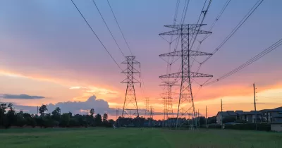 Electricity towers against sunset sky with green trees in background.